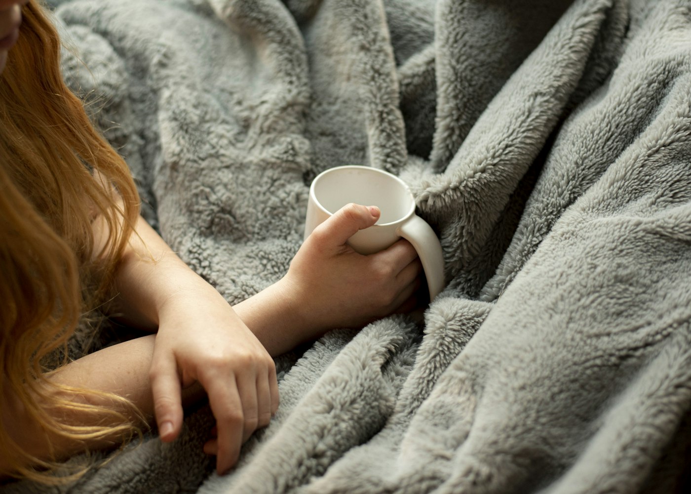 Warm cup of tea, water, and a cozy blanket on a windowsill suggesting comfort and rest