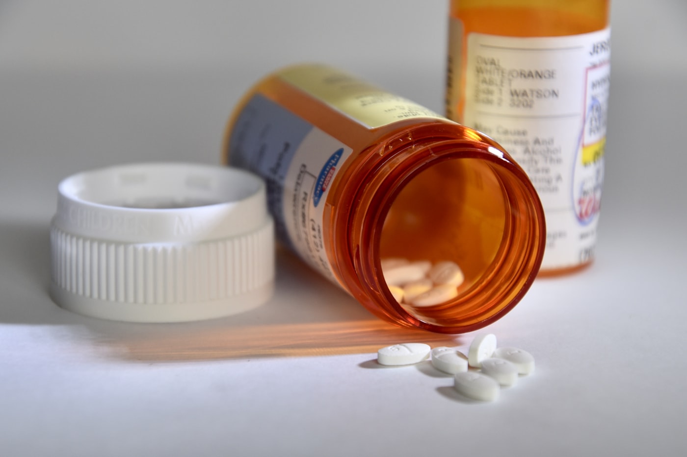 Assorted prescription pill bottles beside a glass of wine on a table
